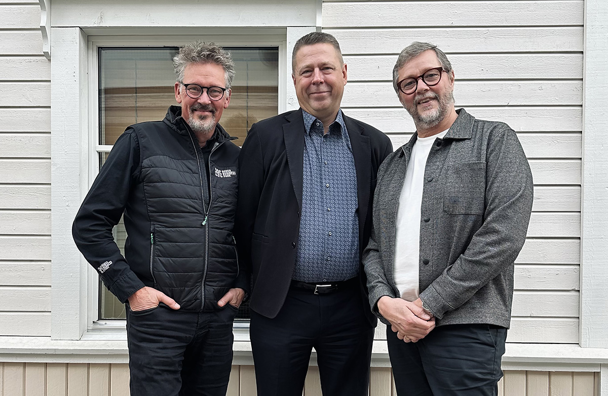 Tre män står framför en vit träfasad och ler mot kameran. Personen till vänster bär svart jacka med Boden Business Park-logotyp, den i mitten bär kostym, och den till höger är klädd i grå skjorta över en vit t-shirt.